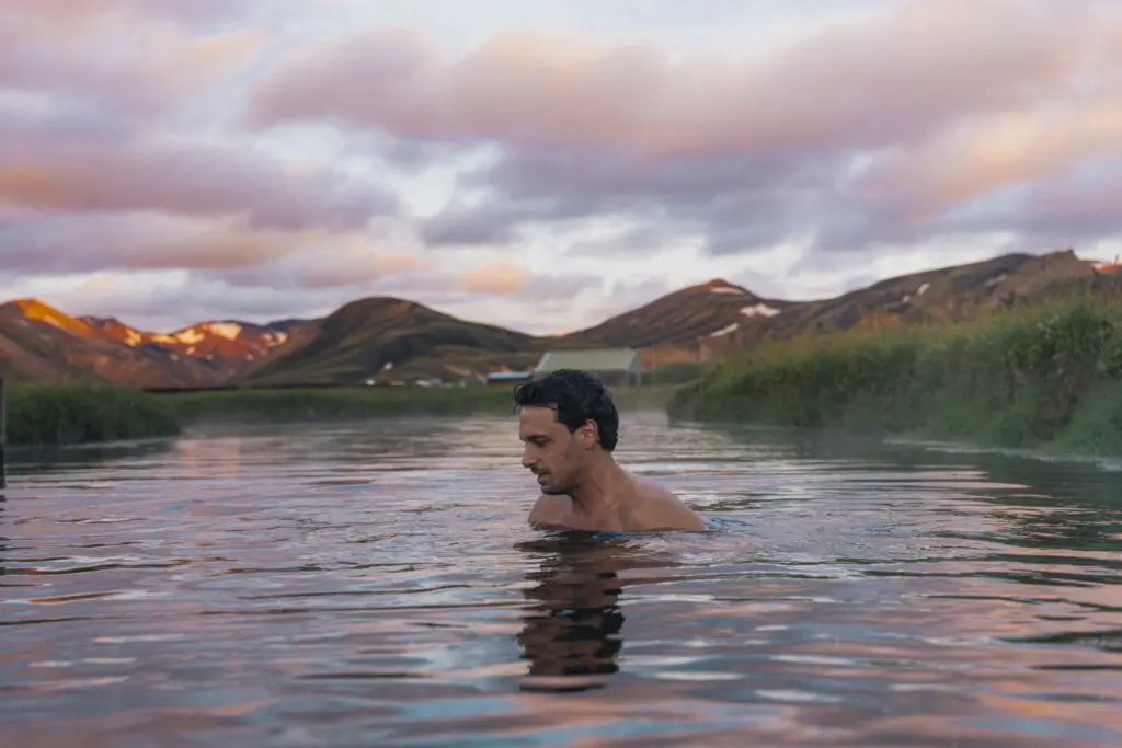 man bathing in a hot spring with mountains at sunset