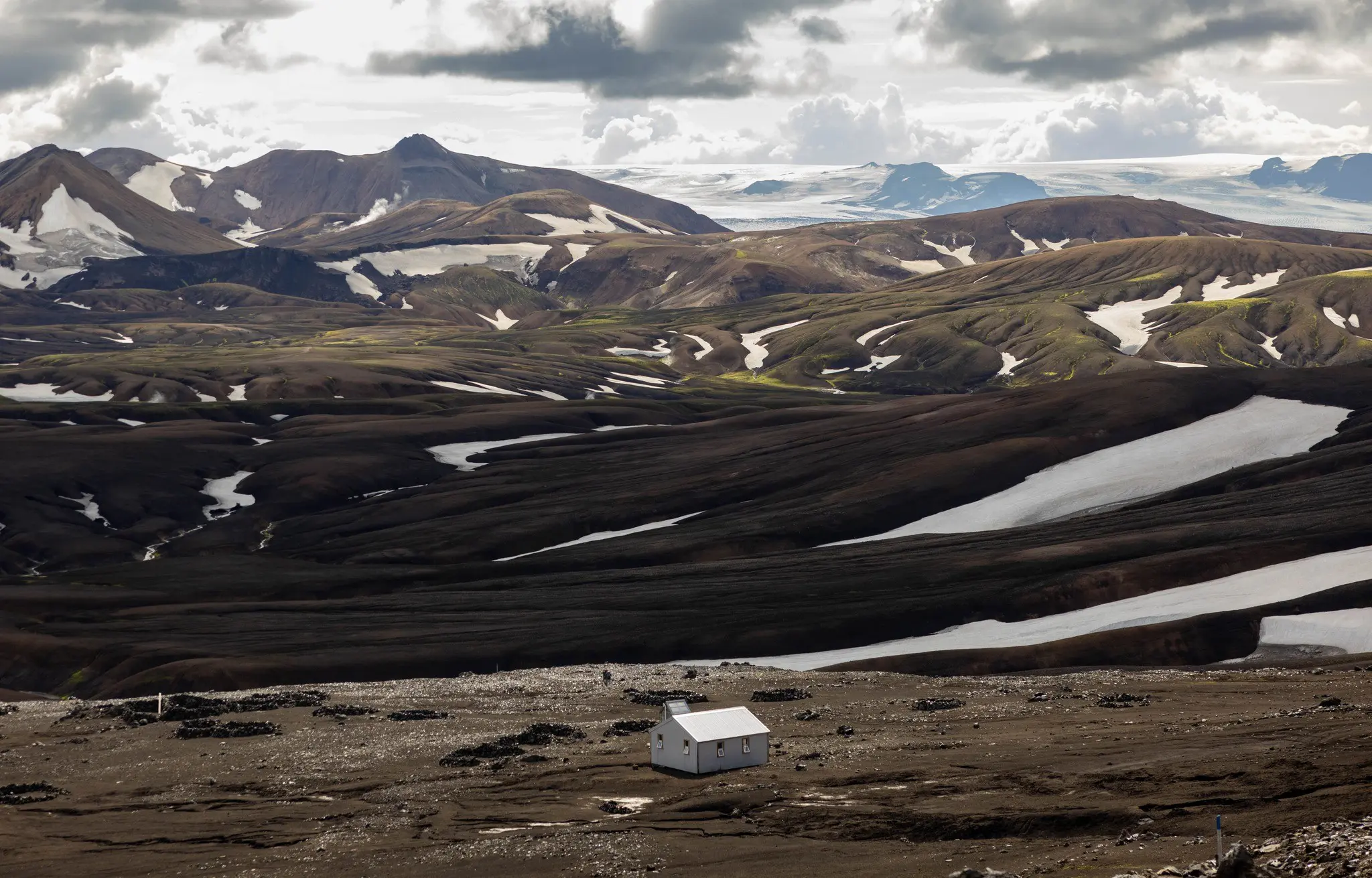 small white hut in vast volcanic landscape with snow patches